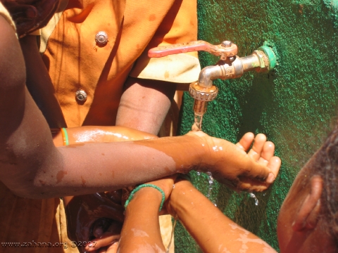 washing hands at communal green water faucet